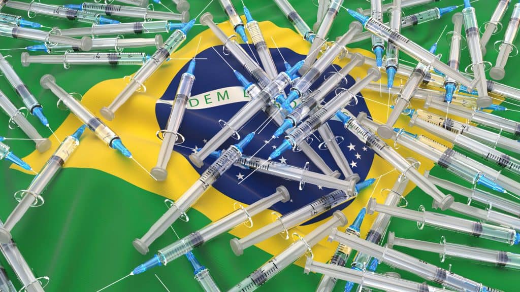Diversas injeções com vacinas contra Covid-19 e ao fundo uma bandeira do Brasil