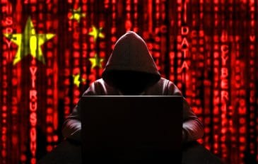 Imagem mostra um homem encapuzado, com o rosto escurecido, à frente de um computador. Atrás dele, a bandeira da China é exibida