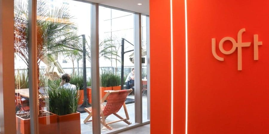 Imagem mostra a entrada do escritório da startup Loft, com o logotipo da empresa na parede laranja.