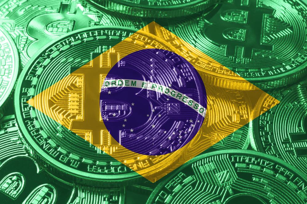 Imagem de uma bandeira do Brasil, com um bitcoin em relevo.