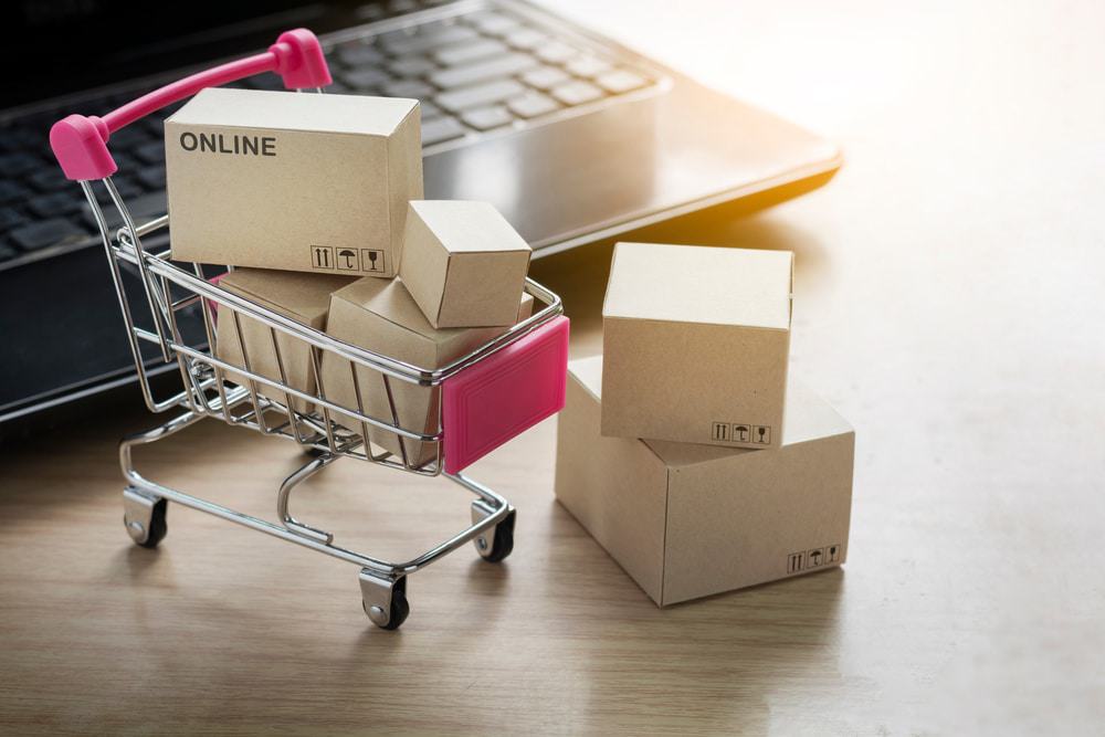 Carrinho de compras cheio de caixas ao lado de um notebook ilustrando o conceito de e-commerce