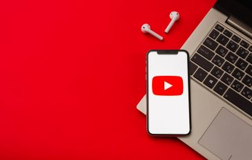 Imagem mostra logo do youtube na tela de um smartphone que, por dua vez, encontra-se em cima de um teclado de notebook. O fundo da imagem é vermelho