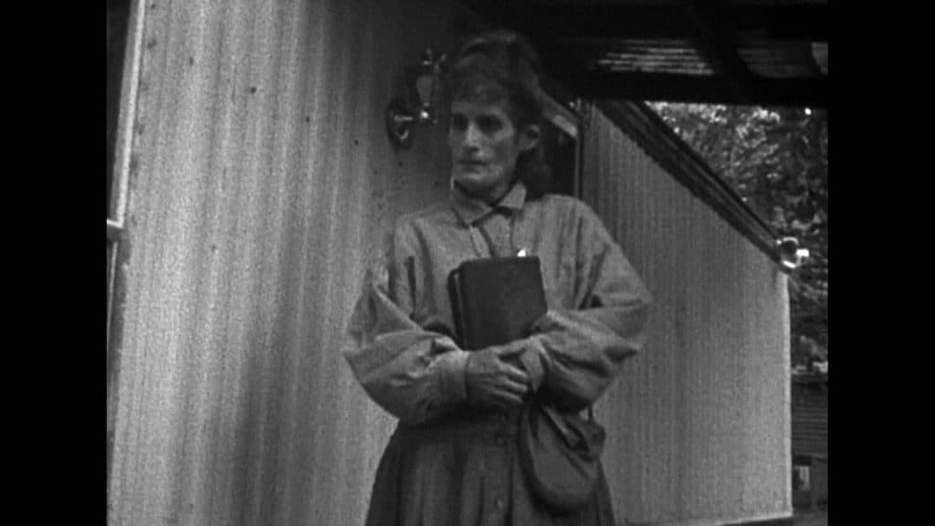 Imagem em preto e branco mostra idosa segurando livro contra o peito. 