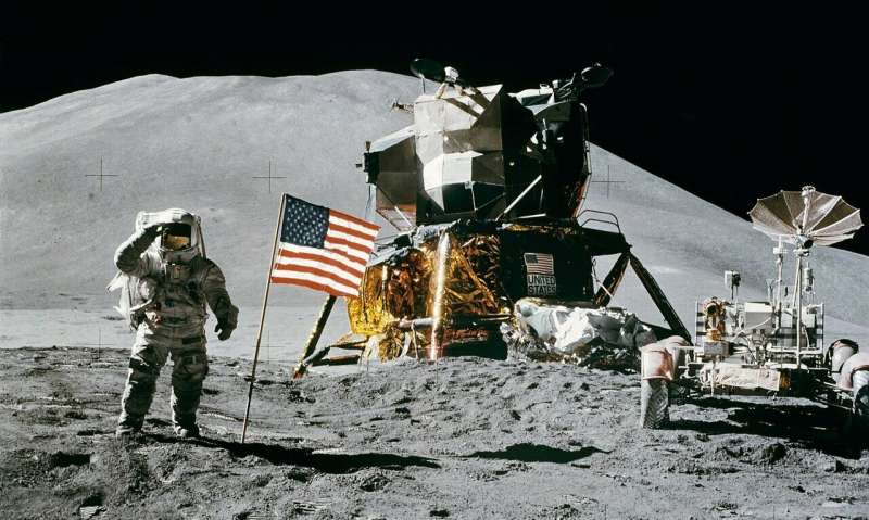 Durante missão do programa Apollo, astronauta saúda a bandeira norte-americana, com módulo lunar e jipe lunar ao fundo