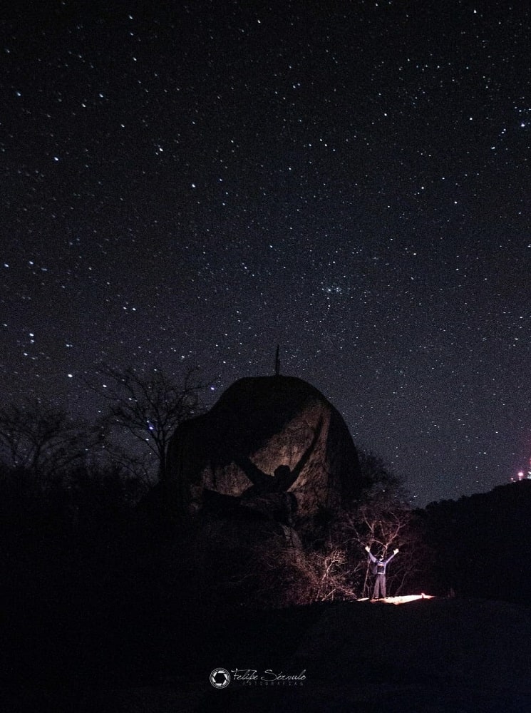 Pedra do Caboclo sob céu estrelado registrada durante trilha noturna
