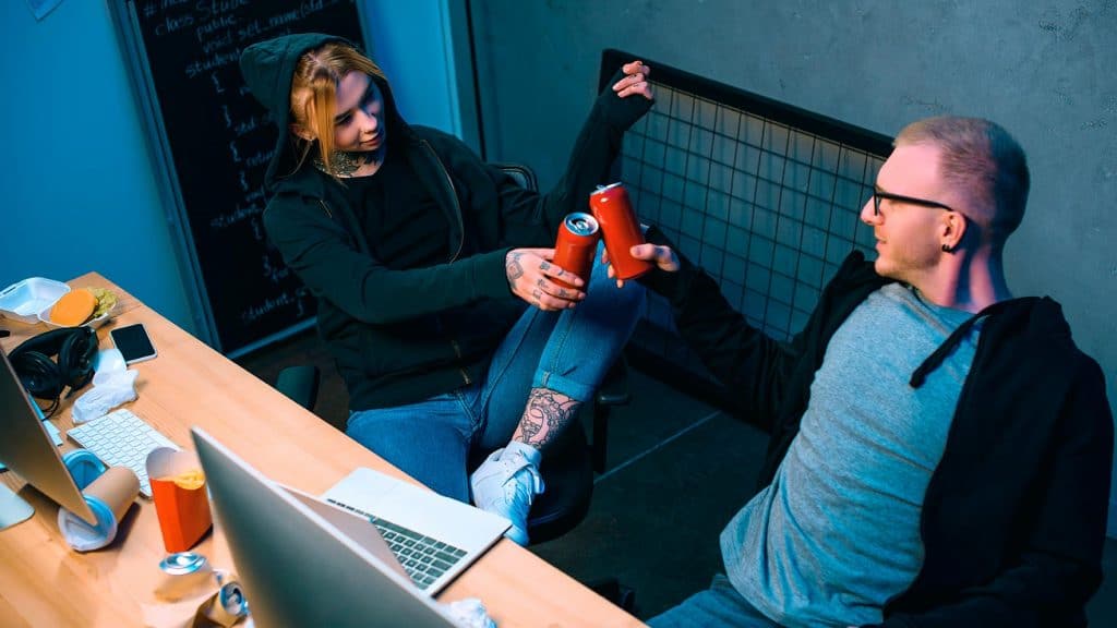 hackers brindando com duas latas de cerveja na frente de computadores