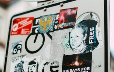 placa de trânsito coberta com adesivos em que um deles é pedindo a favor de Julian Assange