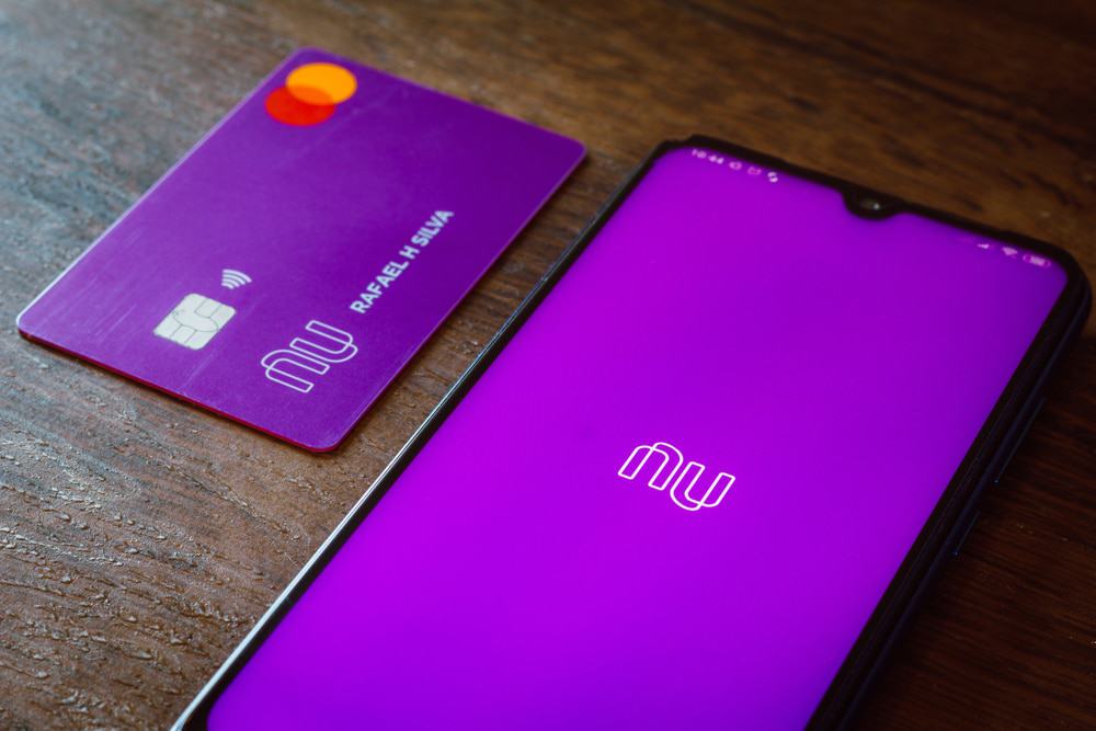 Logotipo do Nubank exibido na tela de um smartphone com um cartão do banco digital ao lado