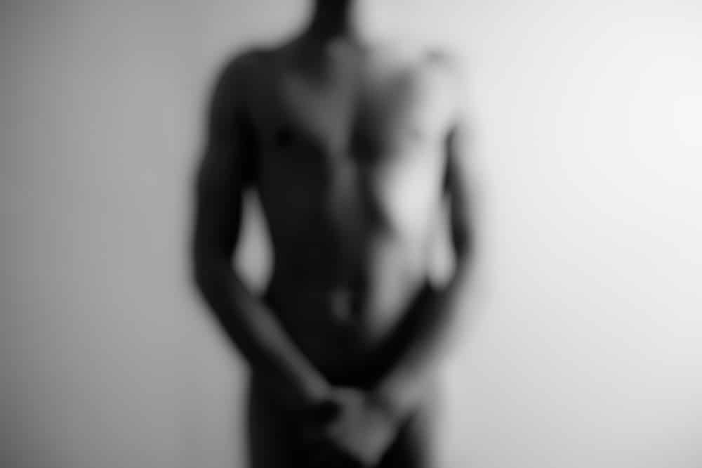 Imagem borrada de homem nu com as mãos nas partes íntimas 