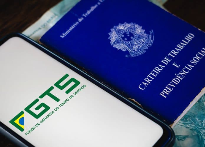 Logotipo do Fundo de Garantia do Tempo de Serviço (FGTS) é visto em um smartphone ao lado da Carteira de Trabalho e Previdência Social do Brasil