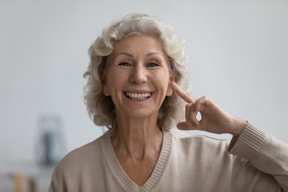 Mulher idosa apontando para a própria orelha