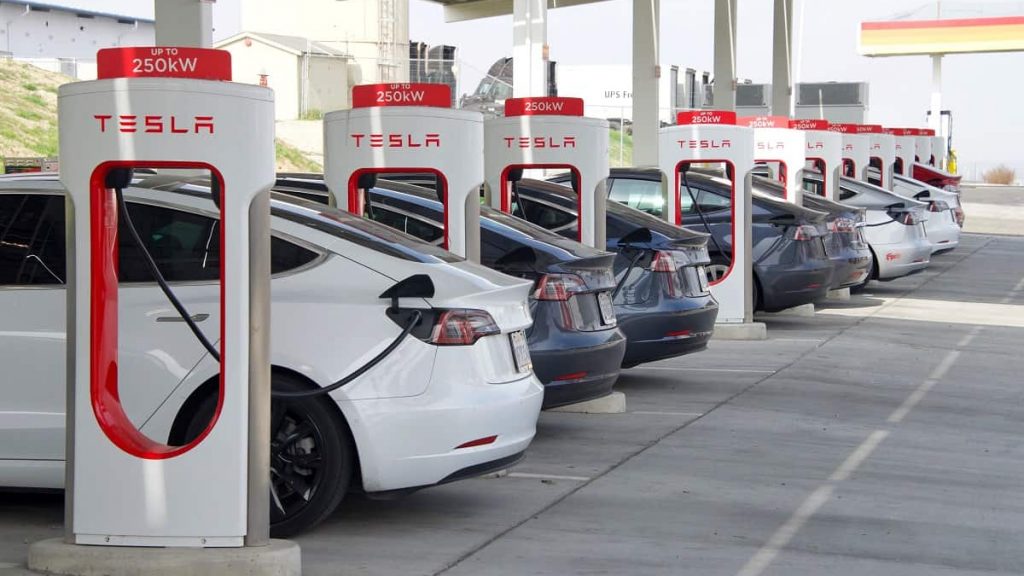 Fileira de carros elétricos conectados em totens de carregamento da Tesla