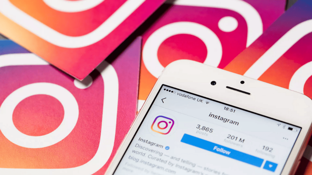 iPhone com página do Instagram no Instagram aberta no aplicativo e, ao fundo, logos do Instagram
