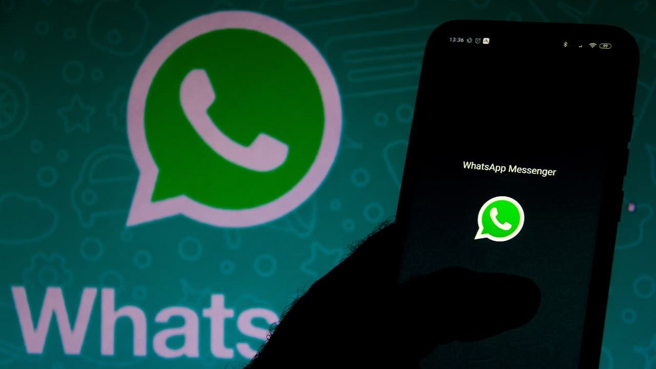 Pessoa segurando celular com logomarca do WhatsApp e, ao fundo, logomarca do WhatsApp